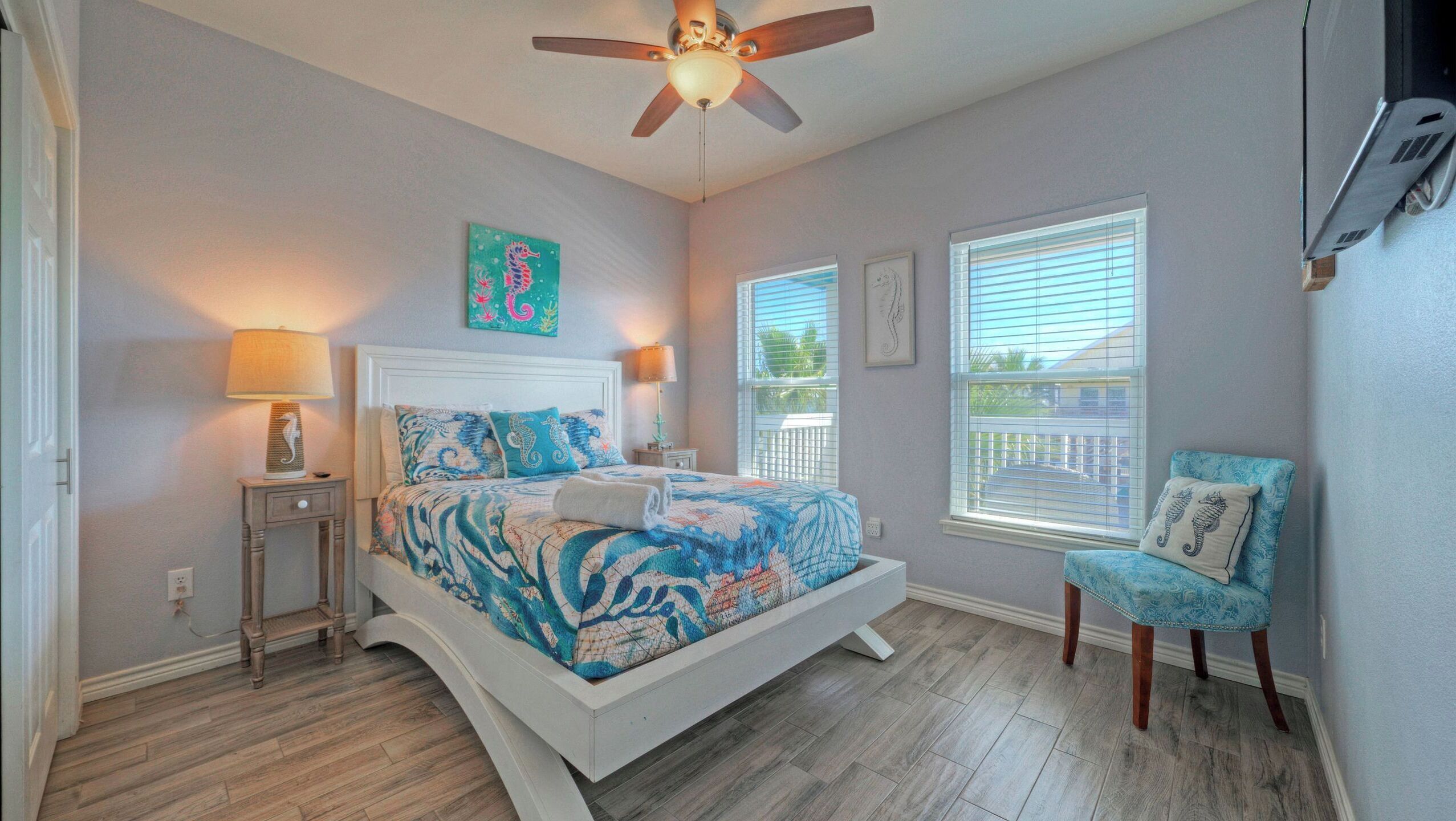 A bedroom with a bed, two bedside tables, a ceiling fan, a window, and a chair.