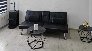 Un salon moderne avec un canapé noir, une table basse ronde, une table d’appoint hexagonale, un ventilateur de plafond et une œuvre d’art murale.