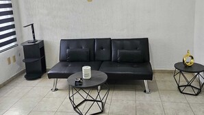 Un salon moderne avec un canapé en cuir noir, une table basse ronde et deux petites tables d’appoint.