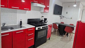 Une cuisine compacte avec des meubles rouges, une cuisinière noire, un évier et un petit coin repas comprenant une table et des chaises.