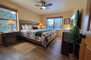 A bedroom with a bed, nightstands, a desk, a television, and a door with a small Christmas tree. - Luxury Forest Cabin | Wild Horses + Starlink (Overgaard)