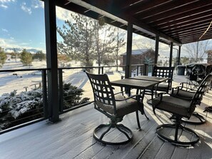 A covered outdoor seating area with metal chairs and a table, overlooking a snowy landscape with trees and distant buildings. - Luxury Forest Cabin | Wild Horses + Starlink (Overgaard)