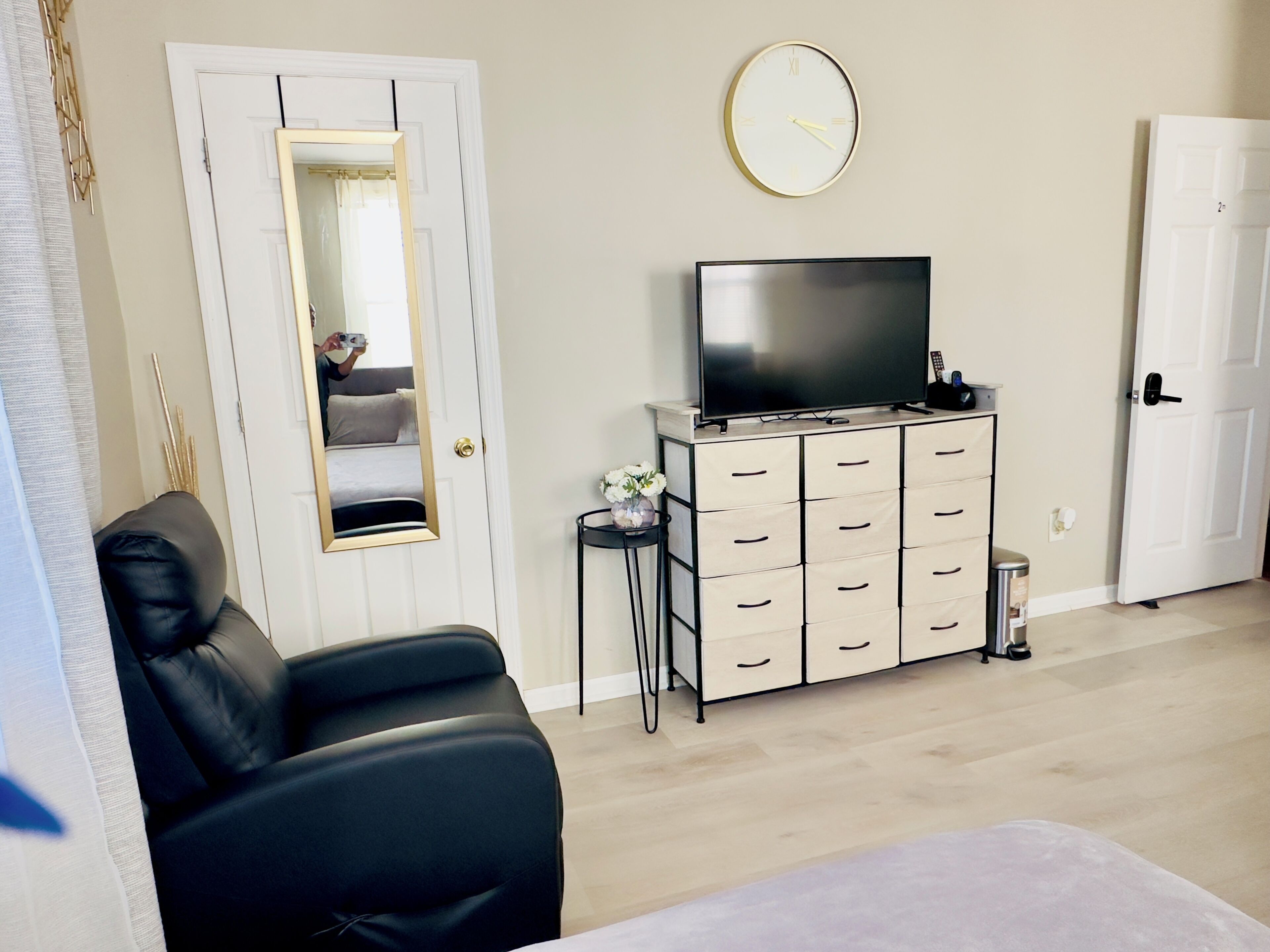 Un dormitorio con una cama, un televisor sobre una cómoda, un espejo y un reloj en la pared.