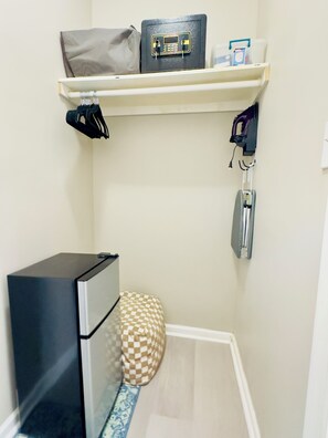 A small room with a desk, a chair, a checkered cushion, a shelf with a bag, a box, and a small electronic device. - Spacious Newark Retreat -2 Full Beds, Workspace & Mini Fridge + AC (Newark)