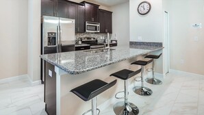 A modern kitchen with dark cabinets, stainless steel appliances, a granite countertop, and bar stools. - Storey Lake Magic - Five Bedroom Villa, Sleeps 10 (Kissimmee)