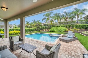 Un espacio al aire libre cubierto con piscina, mobiliario de mimbre y vistas a un barrio residencial.