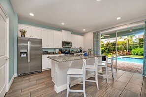 A modern kitchen with a built-in island, white cabinets, stainless steel appliances, and a view of a swimming pool. - Modern 6BR Villa / Games Room/ Private Pool & Spa/10 Min to Disney (Kissimmee)