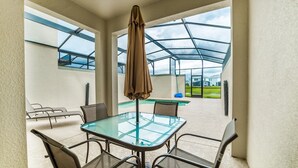An outdoor patio with a glass table and chairs, a covered area with a view of a swimming pool and houses. - Pequod Villa - Four Bedroom Apartment, Sleeps 8 (Kissimmee)