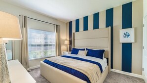 A hotel room with a large bed, a bedside table, a lamp, and a window with blinds. - Pequod Villa - Four Bedroom Apartment, Sleeps 8 (Kissimmee)
