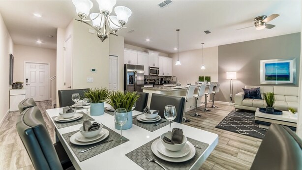 A modern kitchen with stainless steel appliances, a dining area with a white table set for four, and a living room with a sofa and a coffee table. - Pequod Villa - Four Bedroom Apartment, Sleeps 8 (Kissimmee)