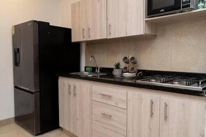 A kitchen with light wood cabinets, a black refrigerator, a stove, and a microwave. - Mint 4 House Old city|Pool|clock tower| (Cartagena de Indias)