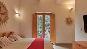 Een slaapkamer met een bed, een houten hoofdbord, een rode sprei, een wandlamp en een raam met uitzicht op bomen.