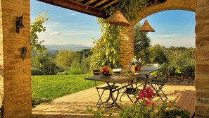 An outdoor patio with a table set for dining, surrounded by greenery and a view of the countryside.