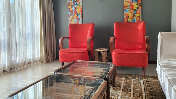 A living room with two red armchairs, a glass coffee table, a beige sofa, and a patterned rug. - Kololo 3BR with Garden, 500m to Acacia Mall (Kampala)