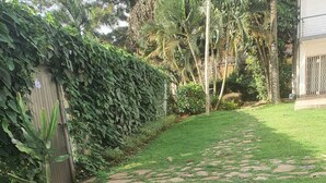 A paved pathway in a garden area with a wooden fence and dense foliage. - Kololo 3BR with Garden, 500m to Acacia Mall (Kampala)