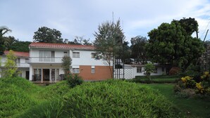 A two-story house with a red-tiled roof, a balcony, and a garden with various plants. - Kololo 3BR with Garden, 500m to Acacia Mall (Kampala)