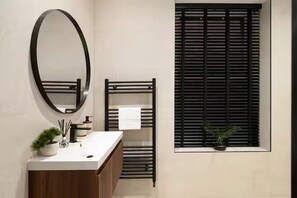 A modern bathroom with a wooden vanity, a round mirror, a towel rack, and a window with blinds. - City Centre Apartment Sleeps 2 With Wifi (Edinburgh)