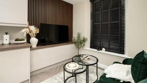 A modern living room with a flat-screen TV, a green sofa, a small coffee table, and a decorative plant. - City Centre Apartment Sleeps 2 With Wifi (Edinburgh)