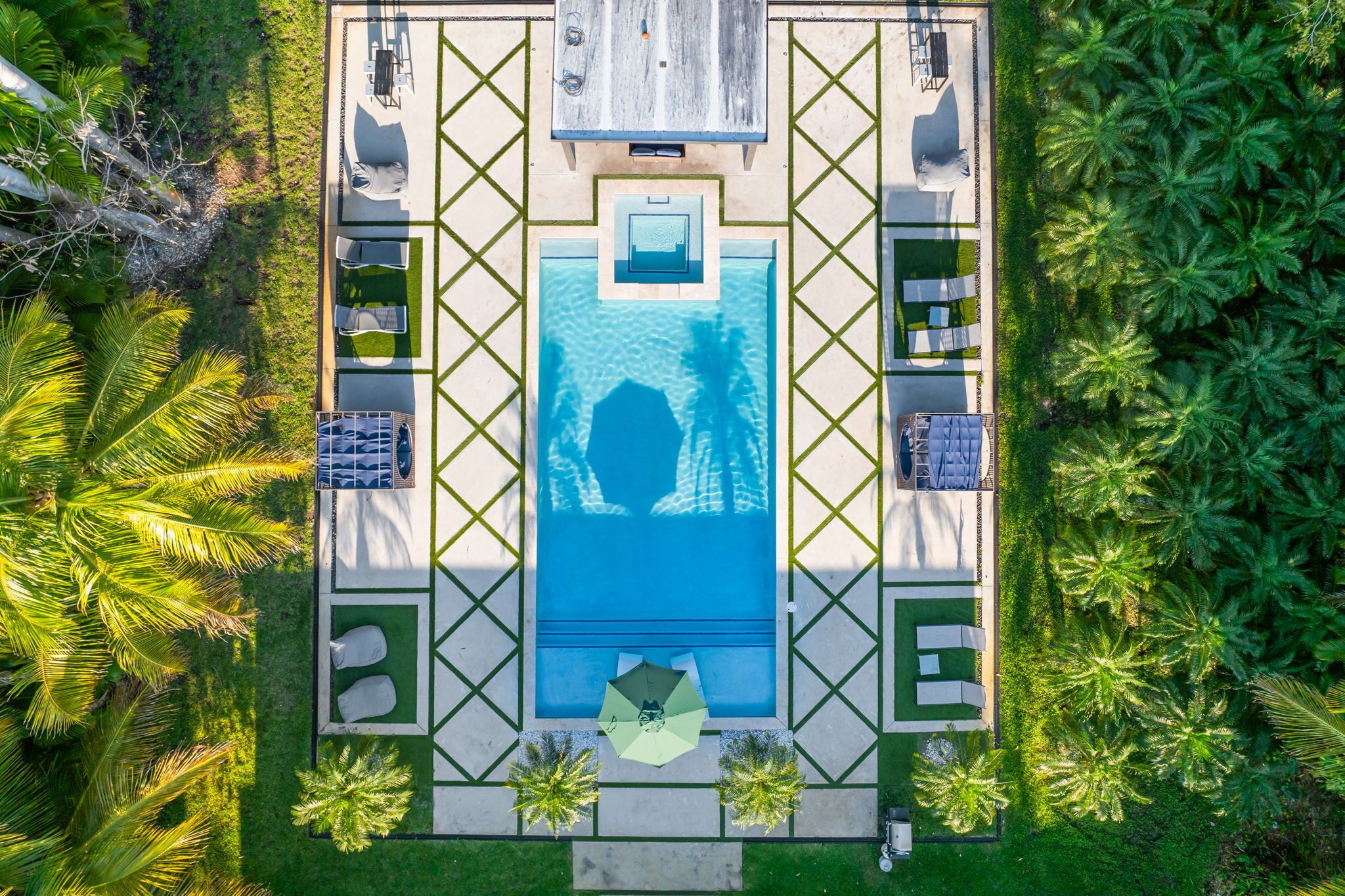 An aerial view of a resort with a central swimming pool, lounge chairs, and palm trees.