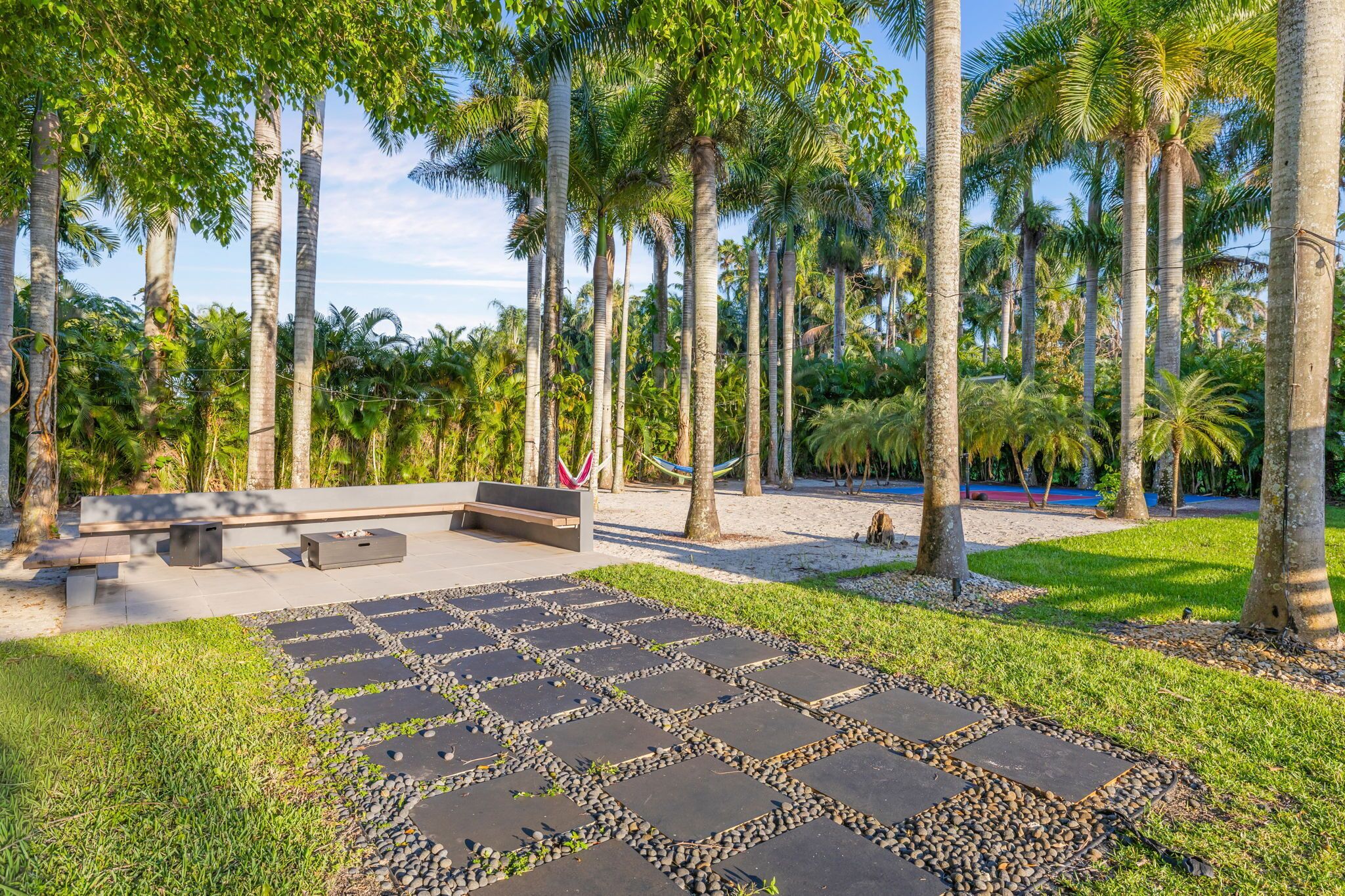 Un jardín tropical con palmeras, un sendero de piedra y mobiliario de exterior.
