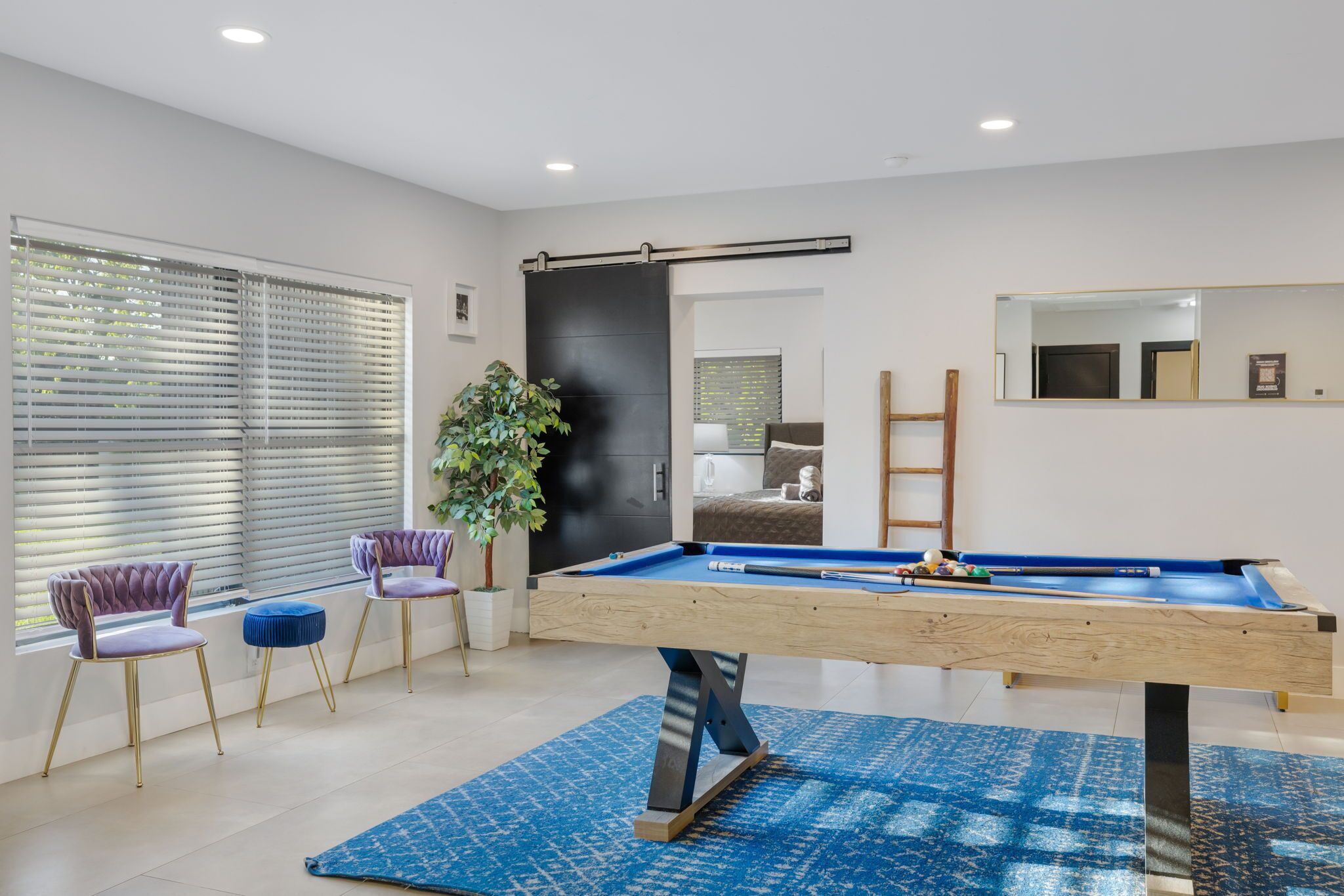 Una habitación moderna con mesa de billar, dos sillas moradas, una planta en maceta y un espejo grande en la pared.