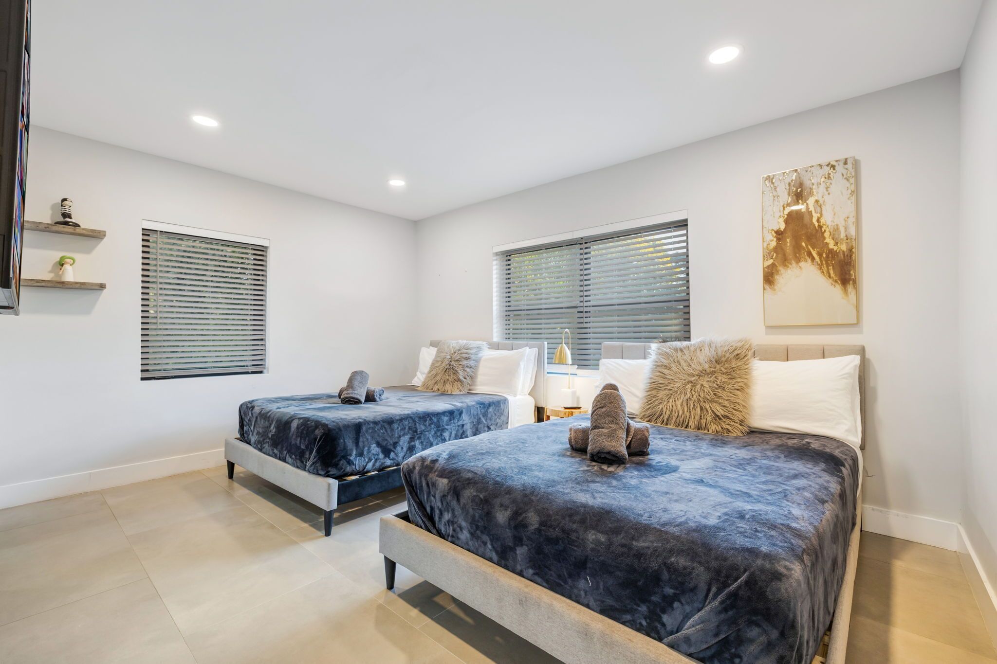 A modern bedroom with two beds, a bedside table, a lamp, and a wall-mounted artwork.