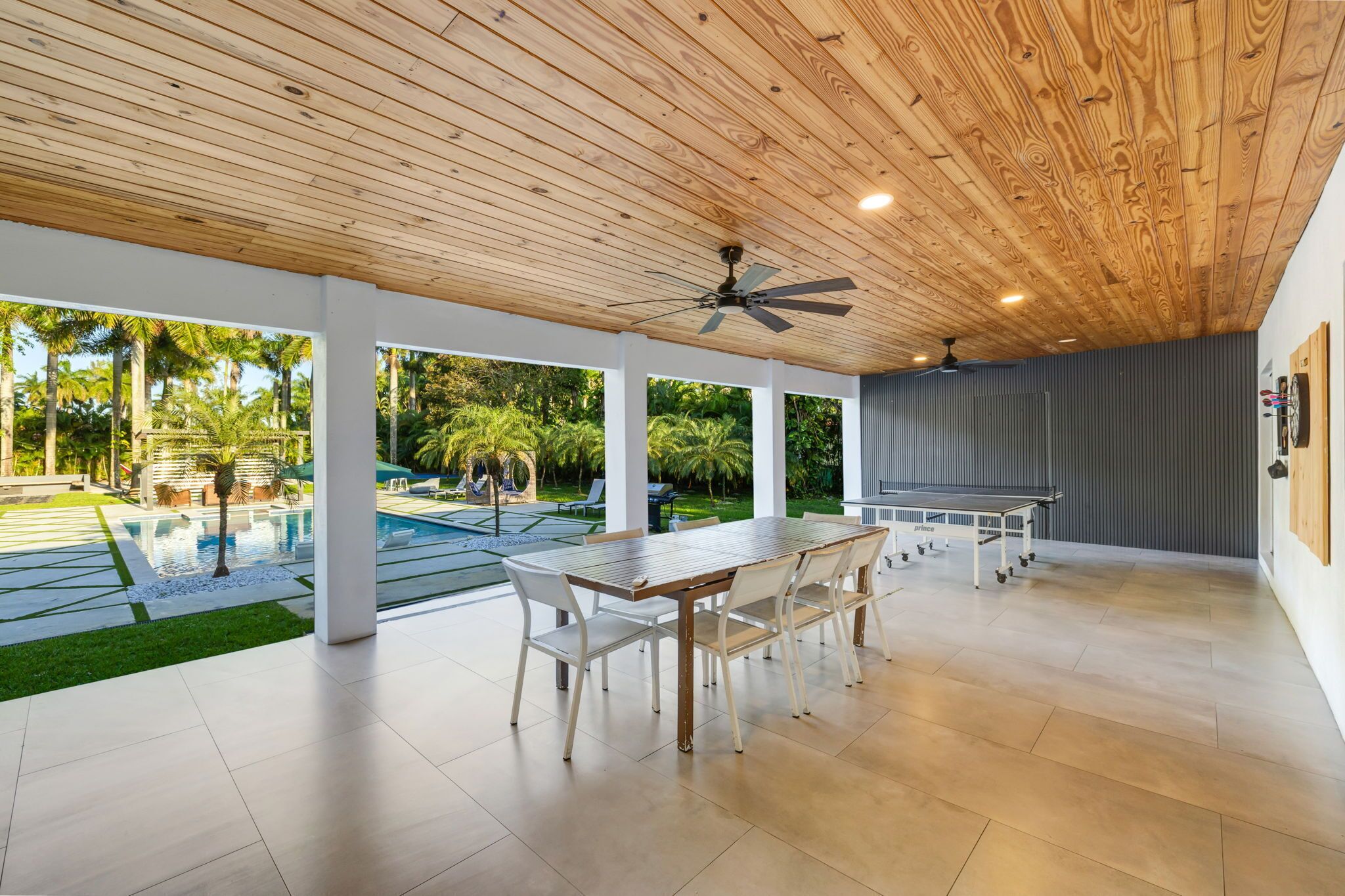 A spacious indoor area with a ping pong table, white chairs, and a ceiling fan.