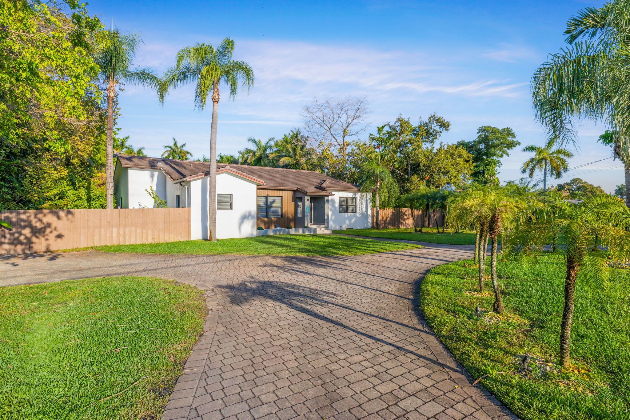 Casa residencial con camino de entrada pavimentado, rodeada de vegetación y palmeras.