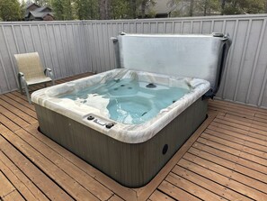 A hot tub on a wooden deck with a chair and a towel.