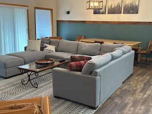 A living room with a sectional sofa, a coffee table, a patterned rug, and a dining area with a wooden table and chairs.