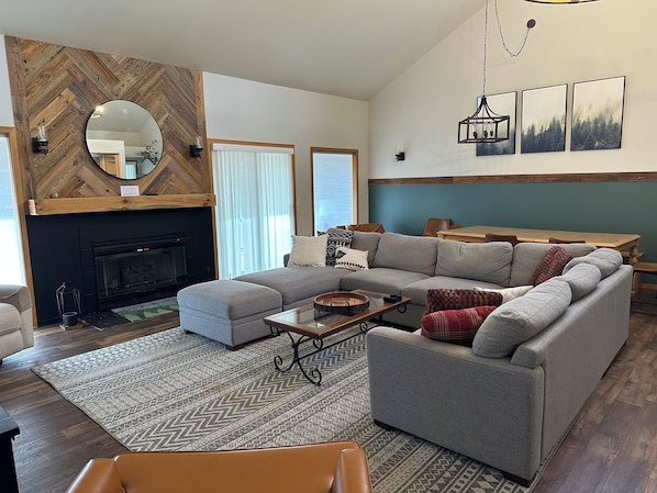 A living room with a fireplace, a sectional sofa, a coffee table, and a dining area with a wooden table and chairs.