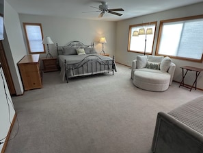 A bedroom with a bed, bedside tables, a chair, a desk, and a ceiling fan.