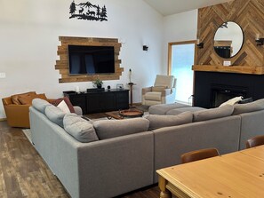 A living room with a sectional sofa, a flat-screen TV, a fireplace, and a dining area.