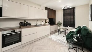 A modern kitchen with white cabinets, a Bosch oven, a sink, and a small dining area with a green sofa and a glass table. - Edinburgh Apartment - Sleeps 2 - Princes St Close (Edinburgh)