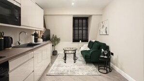A compact living space with a kitchenette, a dining area, and a seating area with a green sofa and a small table. - Edinburgh Apartment - Sleeps 2 - Royal Mile Close (Edinburgh)