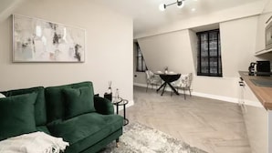 Una sala de estar moderna con un sofá verde, una mesa de comedor con sillas y una cocina con estufa.