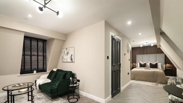 Un espacio habitable moderno y funcional, con un sofá verde, una pequeña mesa redonda y una cama con cabecera.