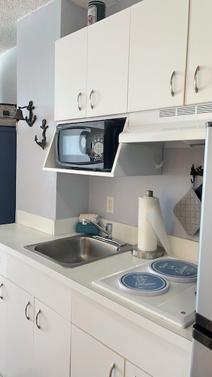 A kitchen with white cabinets, a microwave, a sink, and two decorative plates on the countertop. - DAYTONA BEACHFRONT Condo, Amazing OCEAN Views, Heated Pool, Hot Tub, King Bed (Daytona Beach)