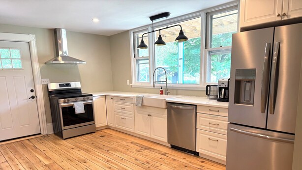 A modern kitchen with white cabinets, stainless steel appliances, and a wooden floor.
