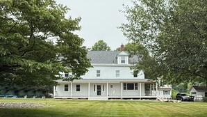 A two-story white house with a porch, surrounded by a well-maintained lawn and trees.