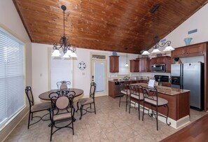 Une cuisine avec un plafond en bois, un coin repas avec des chaises et un réfrigérateur.
