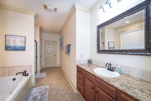 Une salle de bain avec une baignoire, un lavabo, un grand miroir et une porte donnant sur une autre pièce.