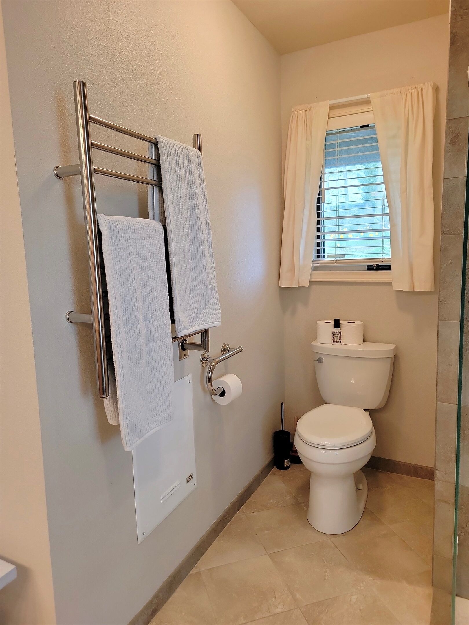 Casa de banho com sanita, um porta-toalhas com duas toalhas, rolo de papel higiénico e janela com cortinas.