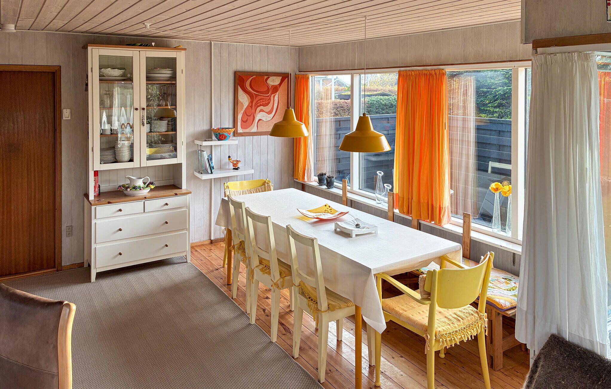 Un comedor con una mesa blanca, sillas amarillas y un mueble con puertas de vidrio.