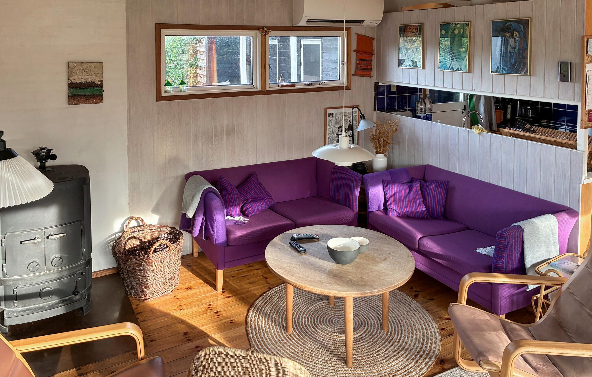 A cozy living room with a purple sofa, a round wooden table, and a wood-burning stove.
