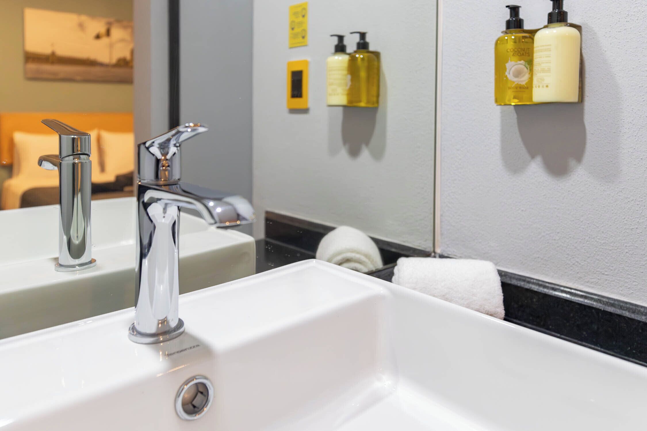 A bathroom with a white sink, chrome faucet, and a mirror reflecting a towel and toiletries.