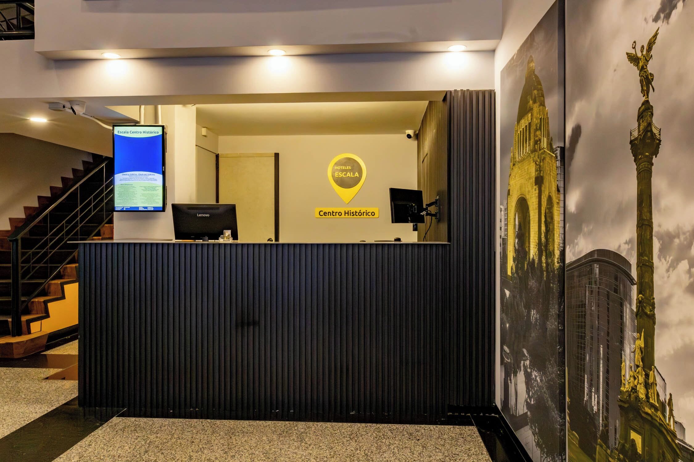 Bancada de recepção com tela digital, placa indicativa do centro histórico e um grande mural de um edifício.