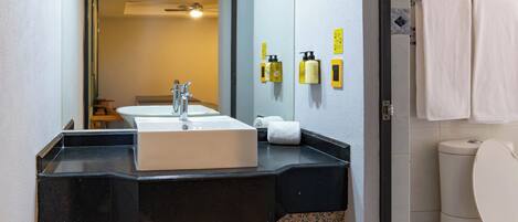 A bathroom with a black granite countertop, a white sink, and a toilet. There are two yellow dispensers on the wall.