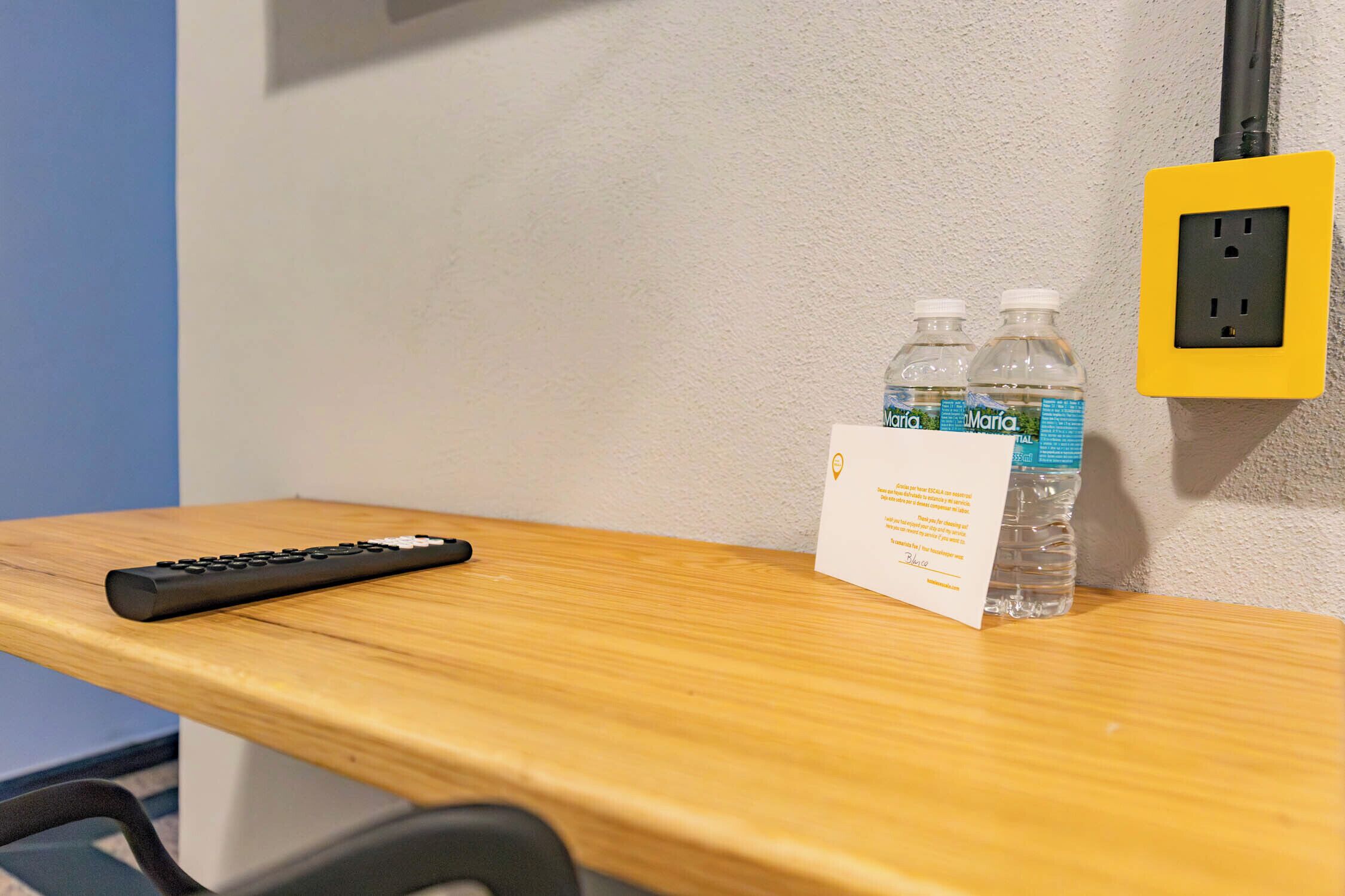 A wooden desk with a remote control, two water bottles, and a card on it.
