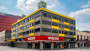 Egy többemeletes épület, amelynek feltűnő, piros és sárga színű üzletportálja van, és a neve „Vazza”.